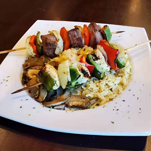 Two beef and vegetable skewers with rice and mushrooms on a white plate at Elmwood Inn.