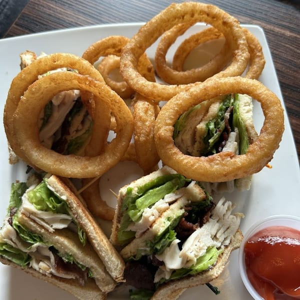 Elmwood Inn's club sandwich with turkey, bacon, lettuce, and onion rings, served with ketchup.
