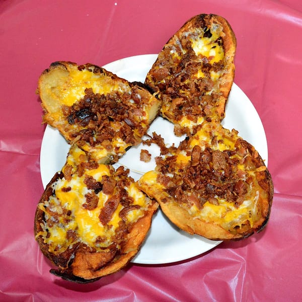 Four Elmwood Inn potato skins, loaded with melted cheese and crispy bacon bits, on a white plate.